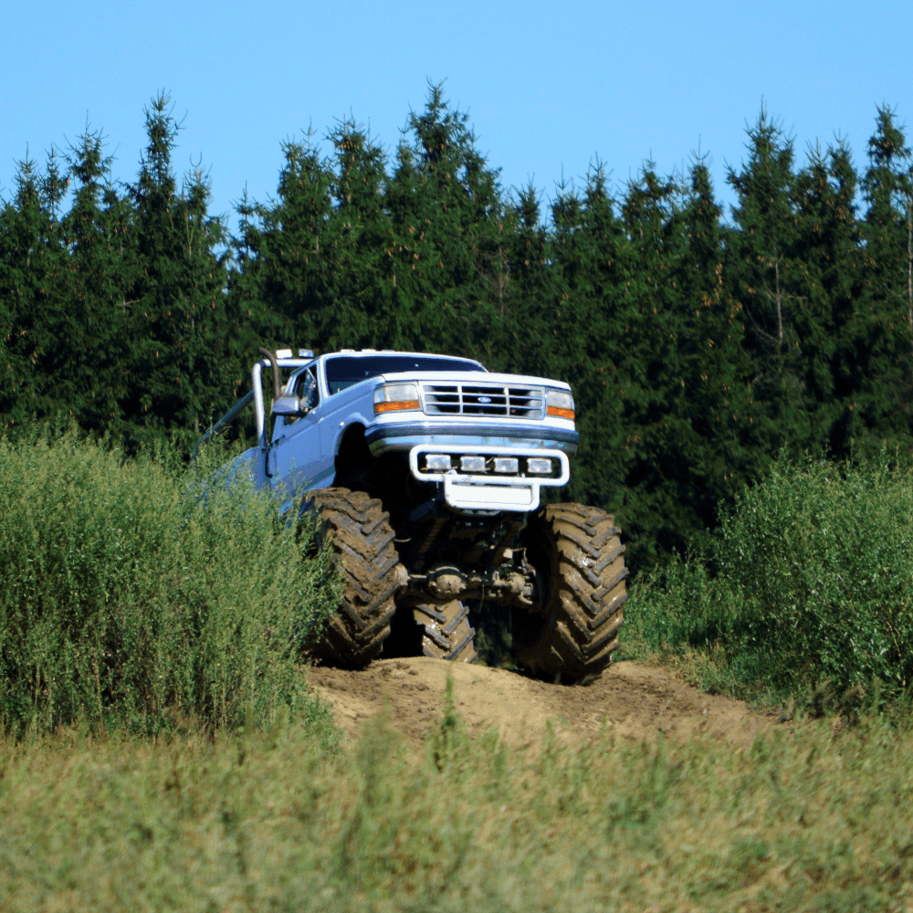 Potężny monster truck przemierza zieloną trasę w leśnym otoczeniu, gotowy na ekscytujące atrakcje dla wszystkich fanów motoryzacyjnych wrażeń.