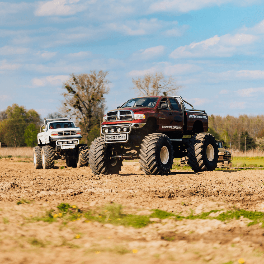 Na obrazie widzimy potężne monster trucki na piaszczystym terenie, z których każdy jest gotowy dostarczyć emocje fanom wszelkiego wieku, na tle malowniczej przyrody okolic Warszawy.