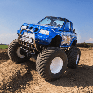 Na zdjęciu widać niebieskiego mini monster trucka w akcji na piaszczystej nawierzchni, idealnego na atrakcje dla pasjonatów motoryzacji w każdym wieku.
