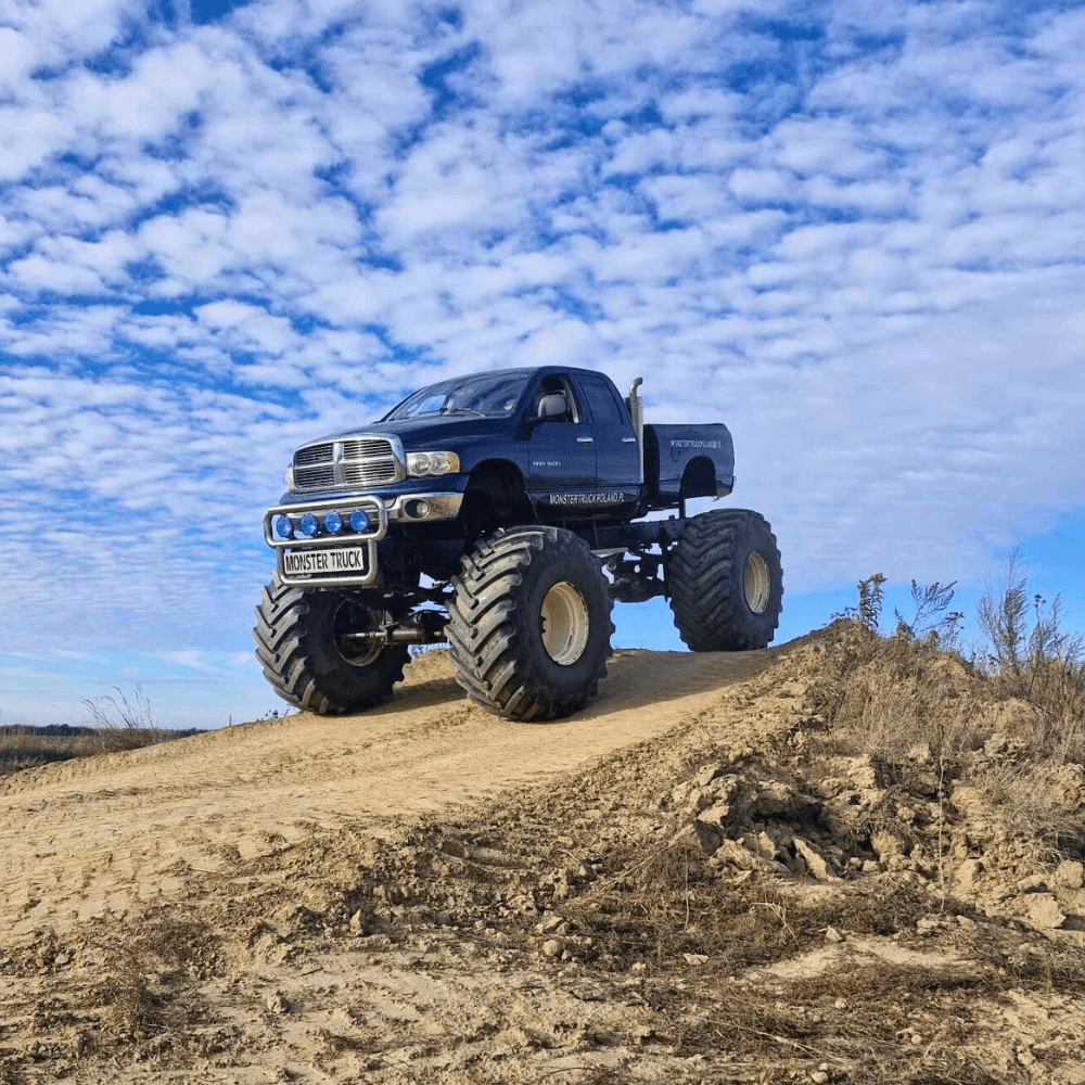Na zdjęciu widać potężny monster truck przemierzający piaszczysty teren pod błękitnym, pochmurnym niebem, zapewniając emocjonujące atrakcje dla wszystkich miłośników motoryzacji.