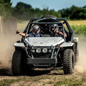 Dwóch kierowców w kaskach emocjonująco pokonuje zakręt w buggy, wzbijając kurz na polnej trasie.