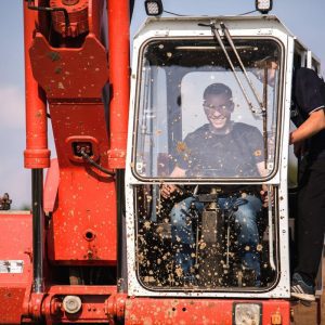Na zdjęciu widać mężczyznę w błotnistej kabinie pojazdu, co sugeruje emocjonującą atrakcję związaną z monster truckami, zlokalizowaną w Gassy koło Warszawy.