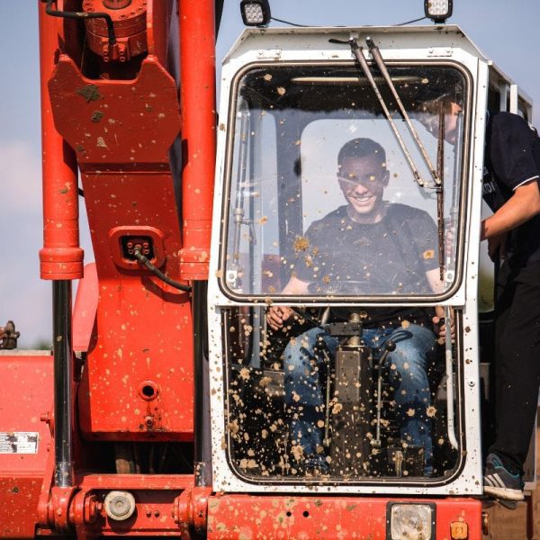 Na zdjęciu widać mężczyznę w błotnistej kabinie pojazdu, co sugeruje emocjonującą atrakcję związaną z monster truckami, zlokalizowaną w Gassy koło Warszawy.