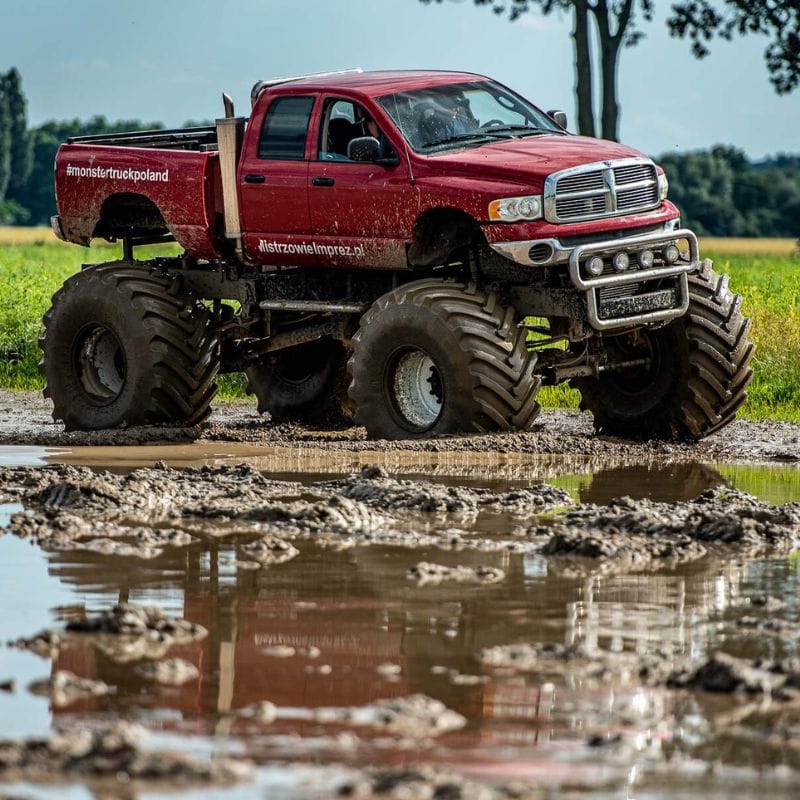 Czerwony monster truck z ogromnymi kołami przemierza błotnisty teren, oferując emocjonujące atrakcje dla wszystkich w Gassach pod Warszawą.