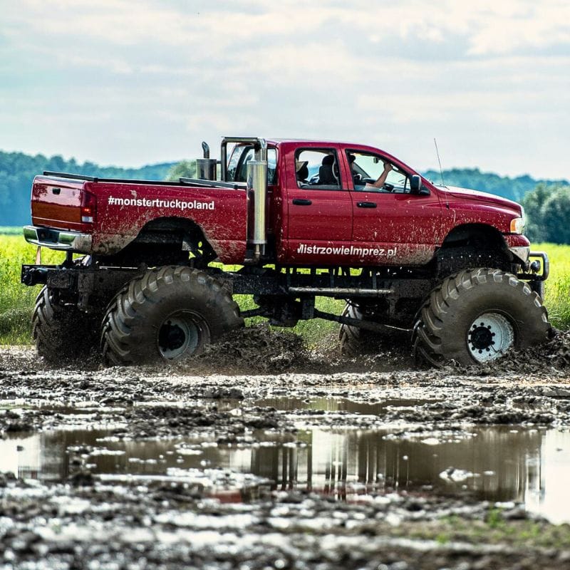 Czerwona ciężarówka monster truck brnie przez błotnisty teren, oferując ekstremalne emocje dla fanów mocnych wrażeń w Gassach pod Warszawą.