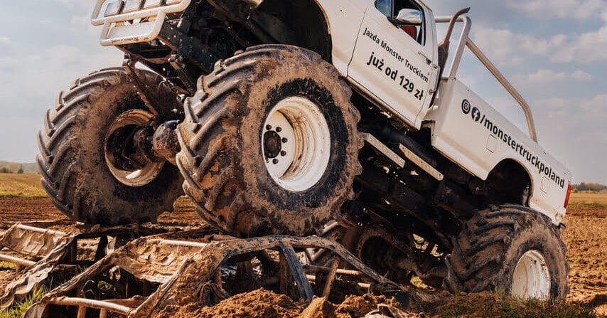 Potężny Monster Truck wznosi się nad wrakami samochodów na błotnistej trasie, promując ekscytujące przejażdżki dla wszystkich w Gassy pod Warszawą.