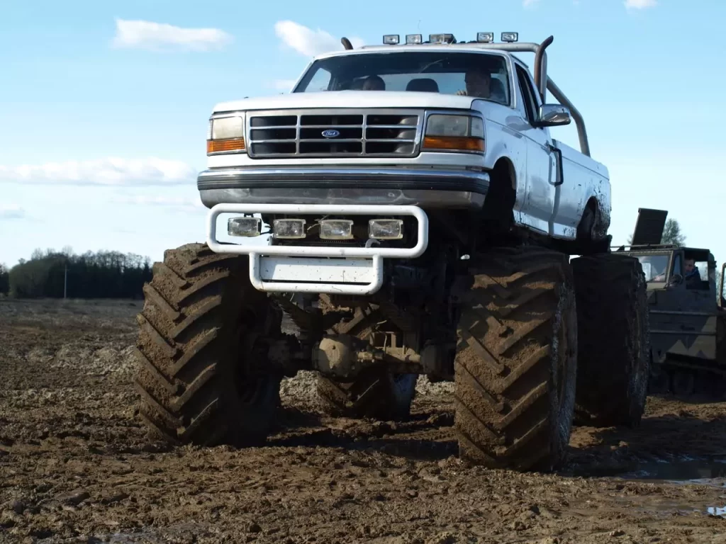 Ogromny monster truck w trakcie jazdy po błotnistym terenie, prezentuje imponujące koła i mocy silnik, co z pewnością dostarcza emocji zarówno dorosłym, jak i dzieciom.