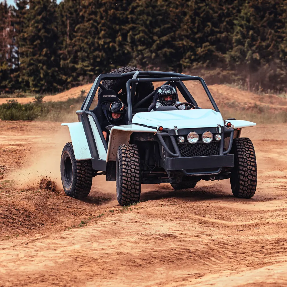 Dwóch uczestników w kaskach pędzi buggy po piaszczystym torze otoczonym zielenią, zapewniając emocje związane z jazdą terenową.