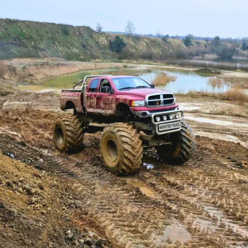 Potężny monster truck przemierza błotnisty teren w malowniczym krajobrazie, symbolizując adrenalinową atrakcję dostępną dla wszystkich poszukiwaczy mocnych wrażeń w okolicach Warszawy.