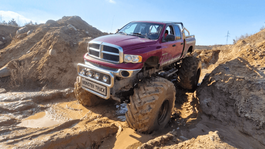 Na zdjęciu widać potężny monster truck przemierzający błotnisty teren, co stanowi niezwykłą atrakcję dla miłośników ekstremalnych pojazdów w każdym wieku.