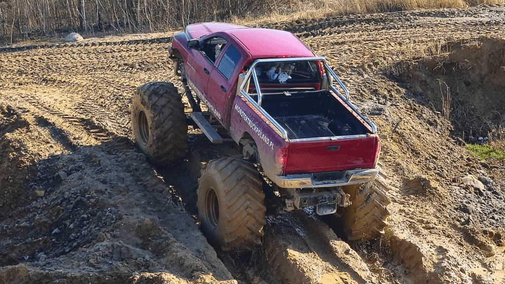 Czerwona ciężarówka Monster Truck przemierza błotnisty teren, podkreślając emocje i przygody dostępne dla wszystkich miłośników ekstremalnych atrakcji w pobliżu Warszawy.