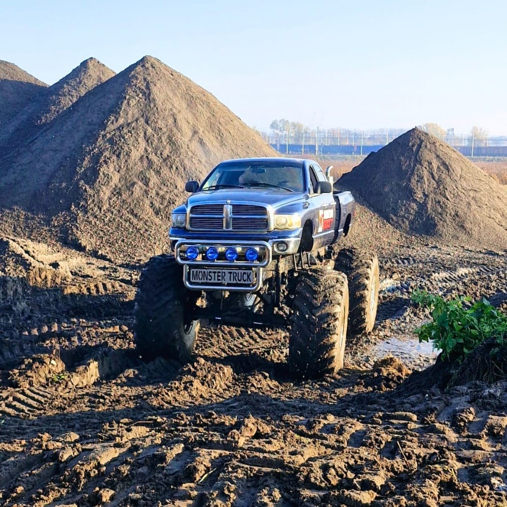 Na zdjęciu widać potężny monster truck poruszający się po błotnistym terenie wśród wysokich kopców ziemi, co zapewnia ekscytujące atrakcje dla wszystkich fanów motoryzacji.