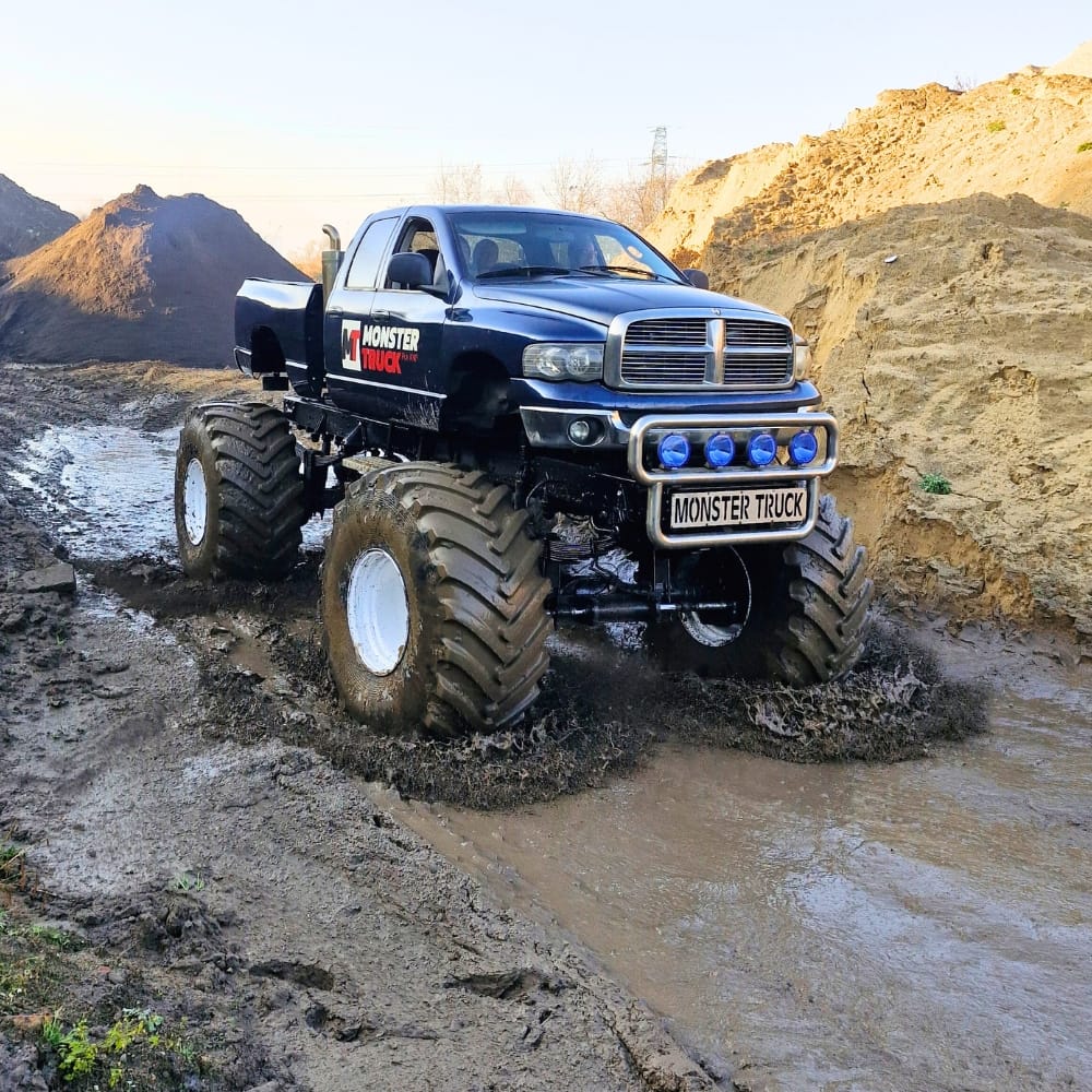 Na zdjęciu widać potężny monster truck przemierzający błotnistą trasę w malowniczym terenie.